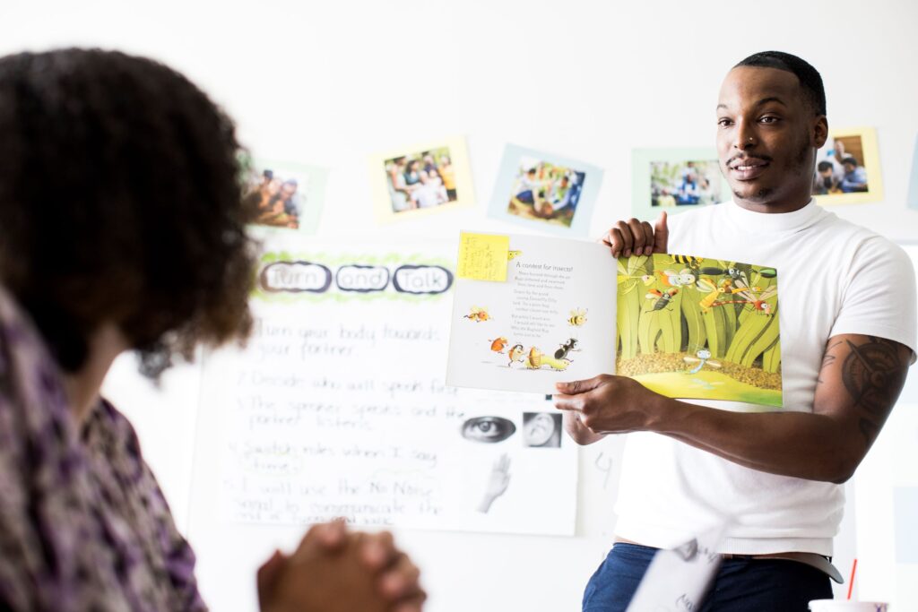 A teacher at the front of a classroom holding up a book to read aloud