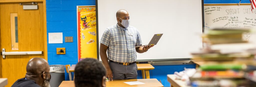 Teaching Fellow alum standing in a classroom coaching current Fellows